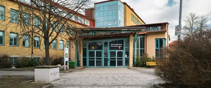 En entré till en skolbyggnad med texten Huvudentré Bjurslättsskolan på glasdörren och en gångväg som leder till den.