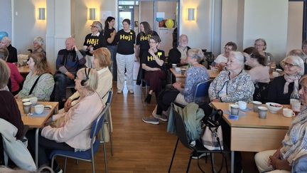 Många intresserade människor tittar mot en föreläsare. I bakgrunden står funktionärer med 