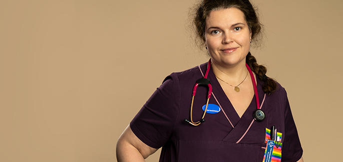 Veronica står mot en beige bakgrund. Hon tittar in i kamera. Runt hennes hals hänger ett stetoskop.