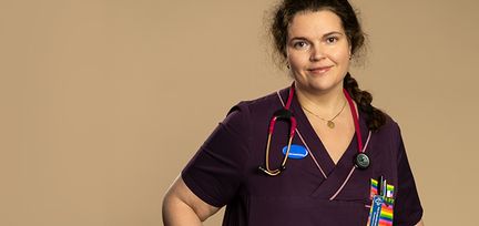 Veronica står mot en beige bakgrund. Hon tittar in i kamera. Runt hennes hals hänger ett stetoskop.