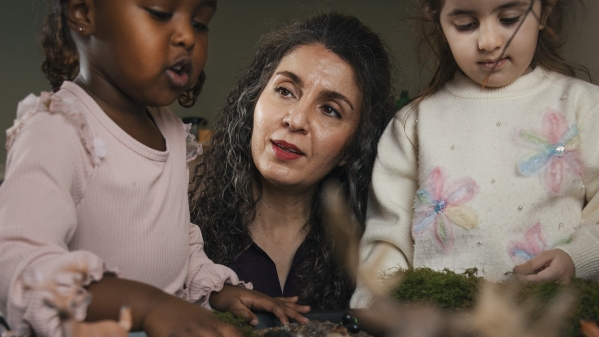 En vuxen är med två barn i förskolemiljö.