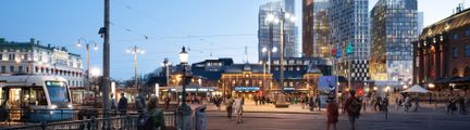 Vallgravens kant i förgrunden brevid en vit byggnad i klassisk stil och centralstationen i bakgrunden.