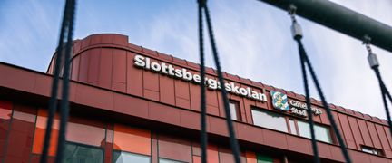 En röd skolbyggnad med texten Slottsbegsskolan på fasaden