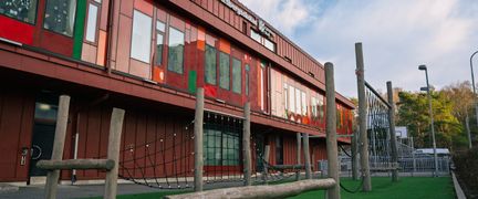 En röd skolbyggnad med en trappa och klätterställning på skolgården