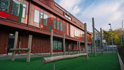 En röd skolbyggnad med en trappa och klätterställning på skolgården