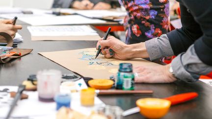 Flera personer ritar och målar vid ett bord.
