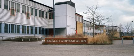 En skolbyggnad med en skylt i cortenstål framför sig med texten Skälltorpsskolan