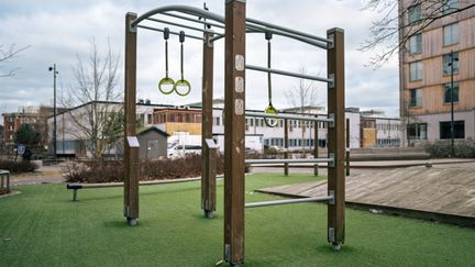 En lekplats med en lekställning med romerska ringar och en skolbyggnad i bakgrunden.