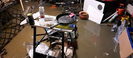 En översvämmad källare med brunt vatten. I det står en sågbänk med bland annat en stekpanna på. 