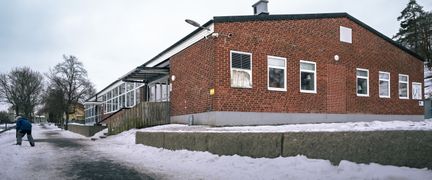 En elev i snön framför en skolbyggnad i rött tegel.