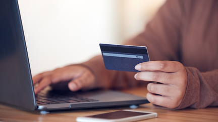 En person skriver på sin dator och håller i ett kreditkort.