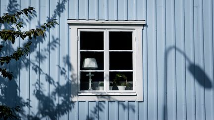 En ljusblå husfasad med ett fönster med lampa i