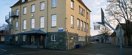 En av Hagenskolans byggnader med en basketkorg och några träd i bakgrunden.