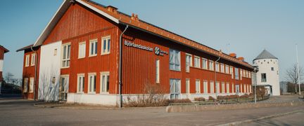 En stor röd skolbyggnad i trä med texten Björlandaskolan på fasaden som står vid sidan av en väg.