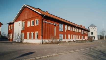 En stor röd skolbyggnad i trä med texten Björlandaskolan på fasaden som står vid sidan av en väg.