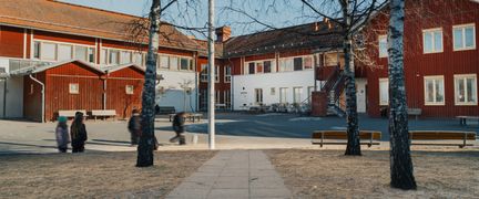 Några elever på en skolgård och en gångväg som leder fram till en röd skolbyggnad.