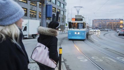 Ett foto av två personer som väntar på att en spårvagn med siffran 6 skall passera.