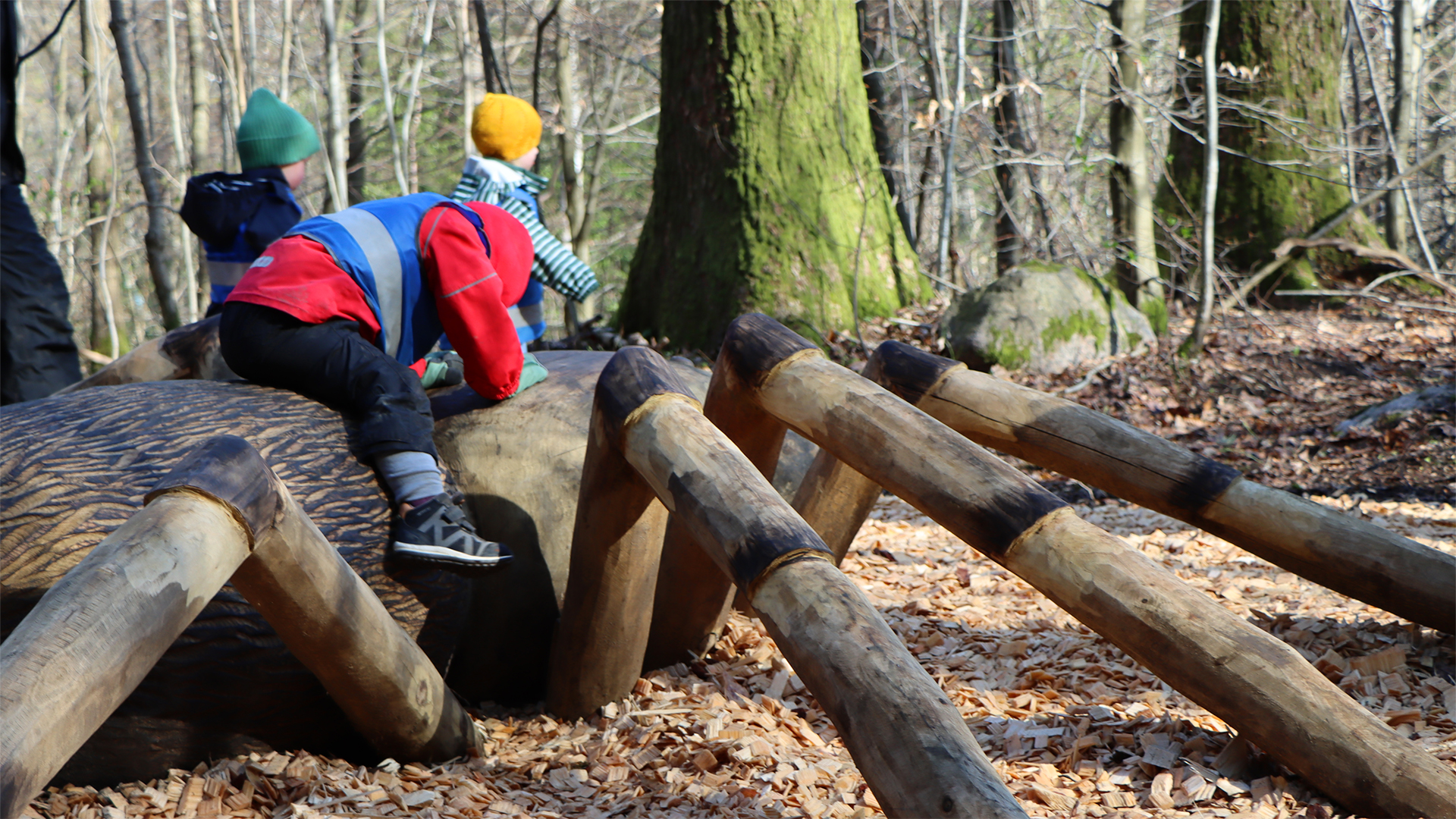 Två barn leker på en träskulptur som föreställer en spindel