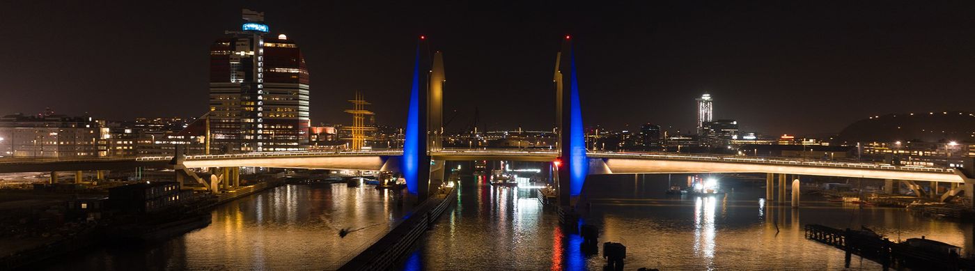 På bilden syns Hisingsbron upplyst med blå och gul belysning mot en mörk kvällshimmel.