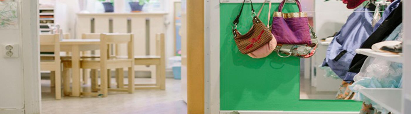 Bild på insidan av en förskolhall, med gröna väggar och väskor som hänger på krokar.