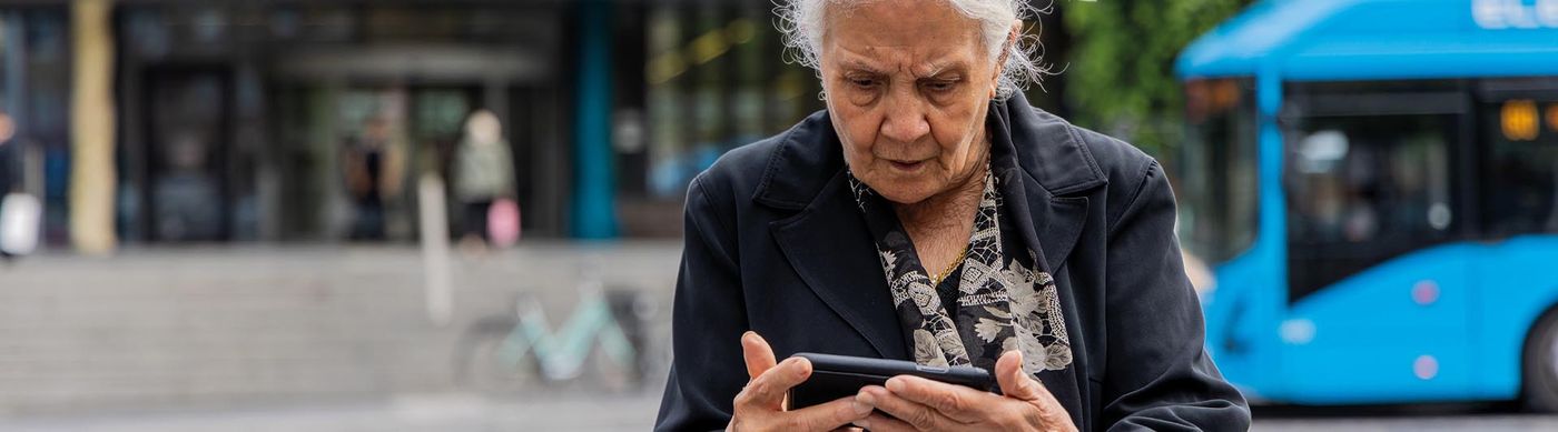 En äldre kvinna soms står i trafiken och kollar sin telefon