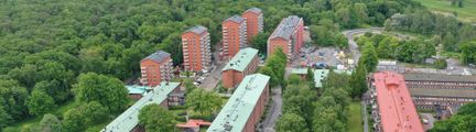Flygvy över byggnader med rödbrunt tegel och ljusgröna metalltak.