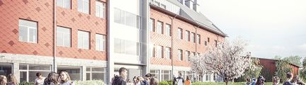 Illustration av skolbyggnad med rödbrun fasad och vita detaljer.