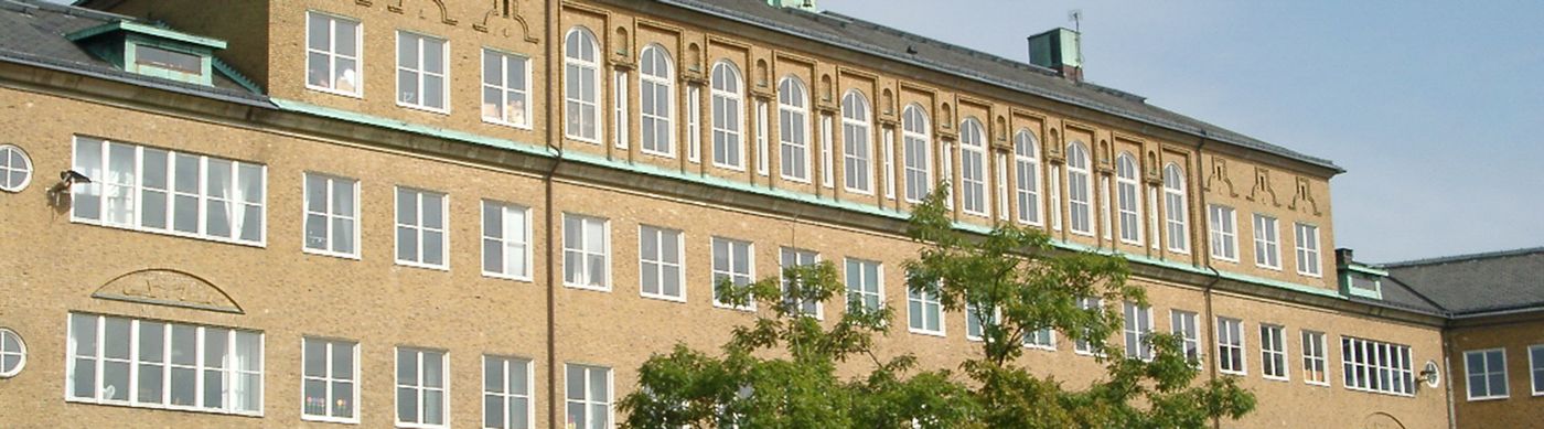 Avlång skolbyggnad i gult tegel och vita fönster.