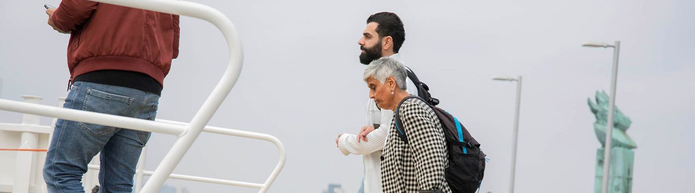 äldre dam får hjälp av yngre man att gå ombord i färja