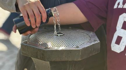 Två personer fyller en vattenflaska vid en dricksvattenfontän.