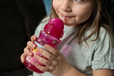 En flicka dricker vatten ur en rosa vattenflaska