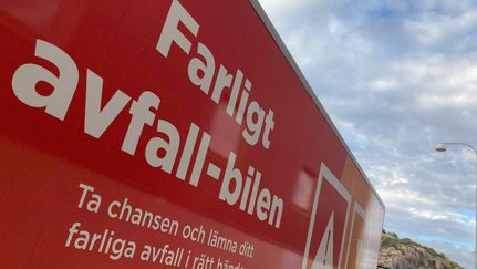 Röd lastbil med texten ”Farligt avfall-bilen” och uppmaning att lämna farligt avfall, fotograferad utomhus mot en molnig himmel.