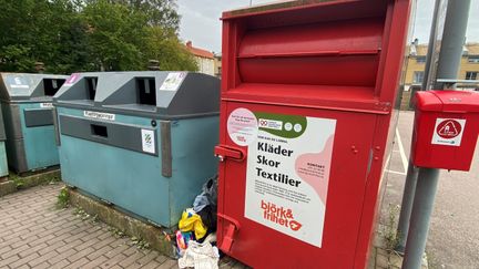 En röd insamlingscontainer för kläder står på Miraalléns återvinningsstation. Vid sidan ligger påsar med kläder. 