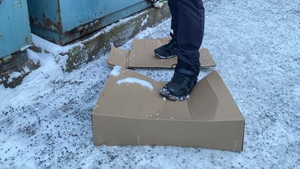 En person stampar till en stor pappersförpackning på en snöig återvinningsstation. 