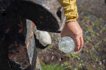En hand sträcker fram en vattenflaska under en dricksvattenfontän