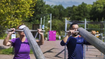 Två personer som lyfter stockar i ett utegym.