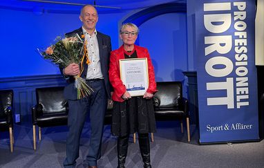 Bild på Johan och Bettan som står med blommor och diplom framför en flagga där det står professionell idrott. 