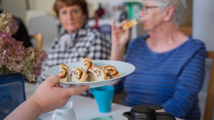 Ett fat med fika är i fokus. i Bakgrunden syns personer sitta och fika. 
