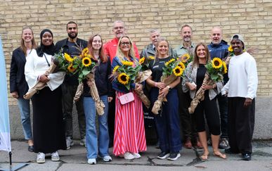 Tolv personer framför en tegelvägg. Vissa håller i blommor.