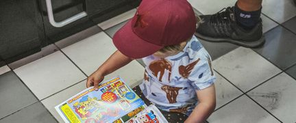 Ett barn som sitter på ett smutsigt klinkergolv och bläddrar i en tidning.