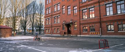 Fjällskolans skolgård med en innebandyplan i fokus. Några barn spelar innebandy i bakgrunden.