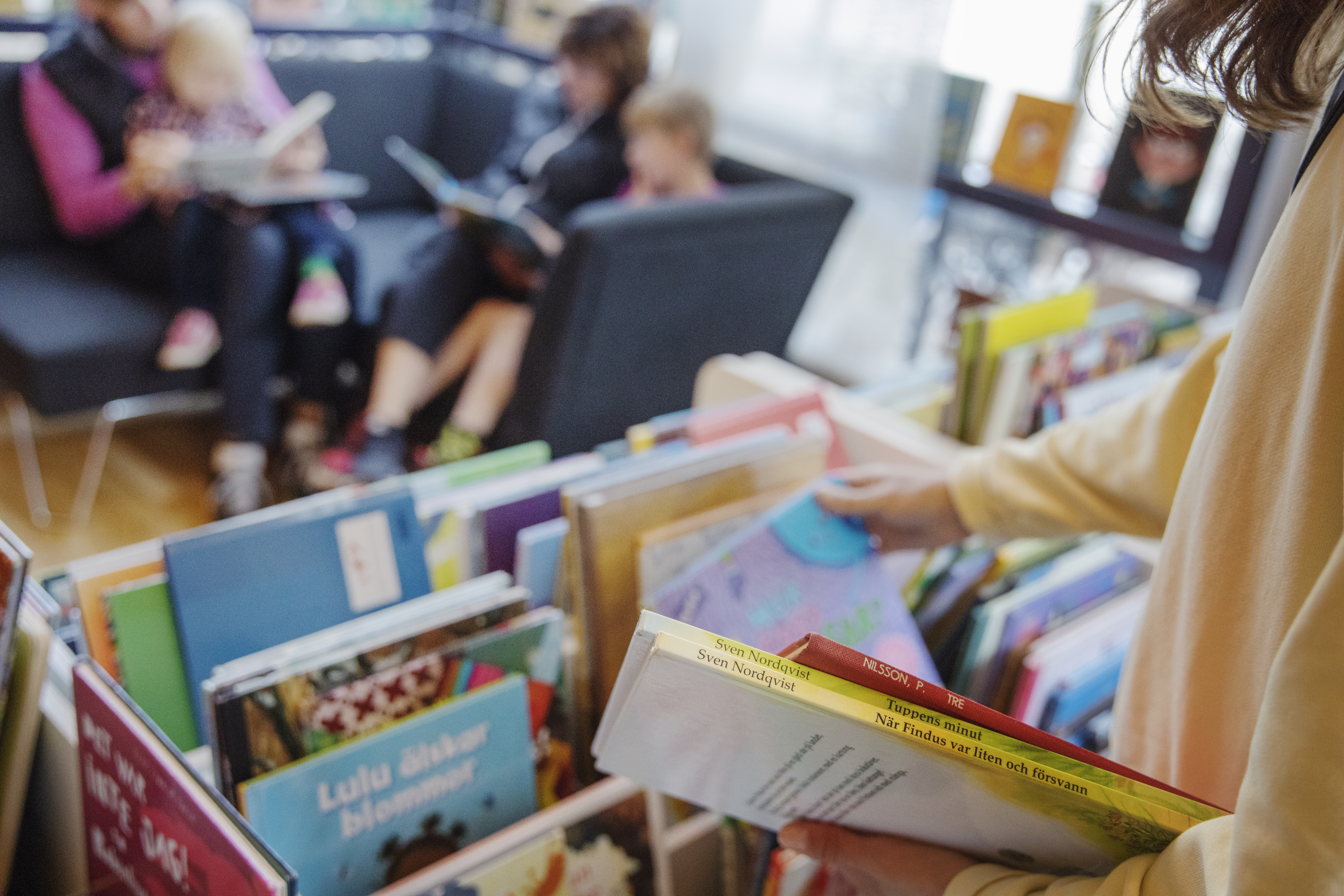 Genrebild. Elev bläddrar bland böcker i en boklåda. Några elever läser i en soffa i bakgrunden.