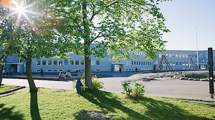 Jättestensskolans huvudbyggnad med skolans skylt och några bänkar i bakgrunden.