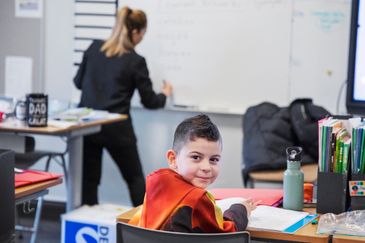 Elever som sitter i ett klassrum och arbetar, en lärare går runt och hjälper eleverna