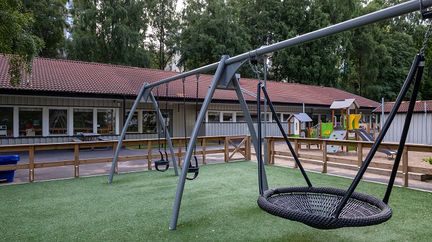 Ett grått enplanshus med en gunga och lekplats framför.