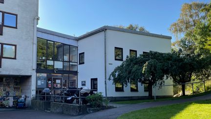 Två vita fyrkantiga hus med ett glasparti emellan, gräsmatta framför och träd vid sidan.