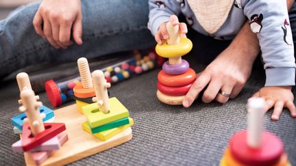 Barn och vuxen leker med träleksaker på golvet.