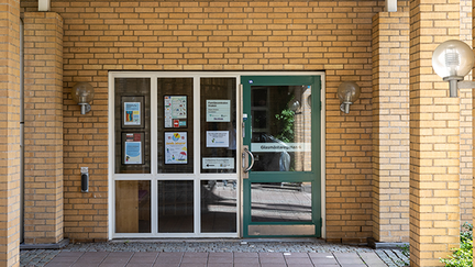 En ingång med grön dörr med fönsterglas omgiven av gult tegel.