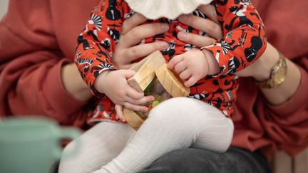 Ett barn sitter i en vuxen persons knä och håller en träleksak. Vi ser inga ansikten.
