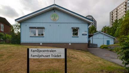 Ett ljusblått trähus på en kulle med skylt framför Familjecentralen, Familjehuset Trädet